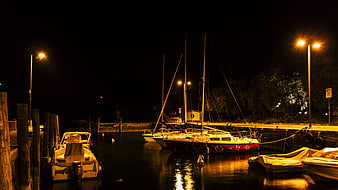 Sailboats docked in a marina at night with warm street lighting