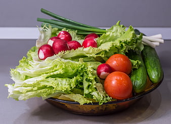 Fresh salad ingredients in a bowl with lettuce, radishes, tomatoes, and cucumbers