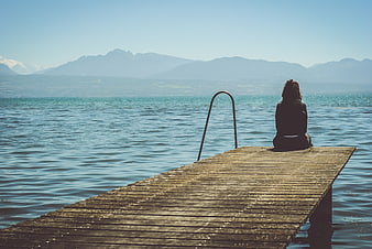 Woman sitting on wooden pier overlooking lake and mountains
