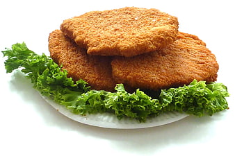Golden Breaded Chicken Schnitzel Stacked on White Plate with Green Lettuce Garnish