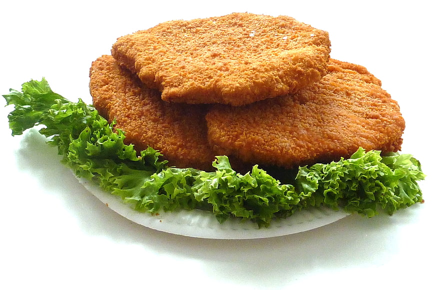 Golden Breaded Chicken Schnitzel Stacked on White Plate with Green Lettuce Garnish