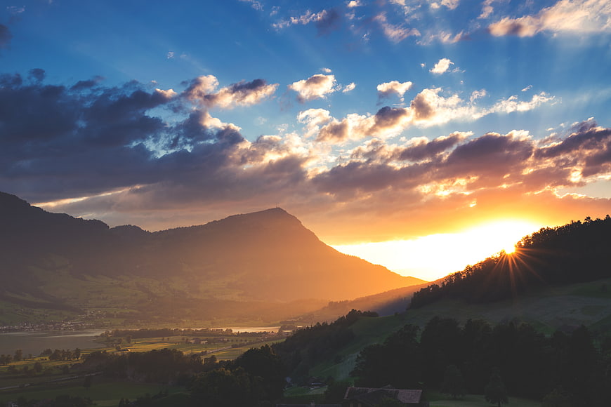 Dramatic sunset over mountain valley with sunburst and clouds