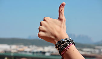 Hand Giving Thumbs Up with Bracelets Against City Skyline
