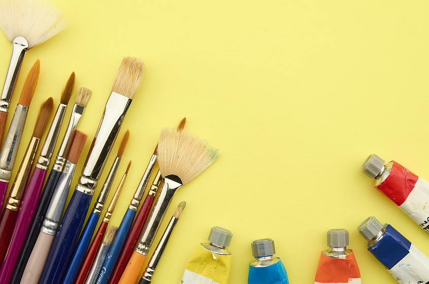 Art supplies and paint brushes on yellow background