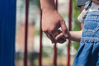 Father holding child's hand outdoors in denim overalls