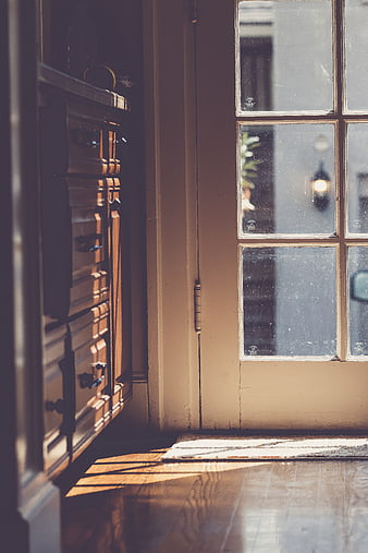 Sunlit wooden floor and vintage dresser near glass door