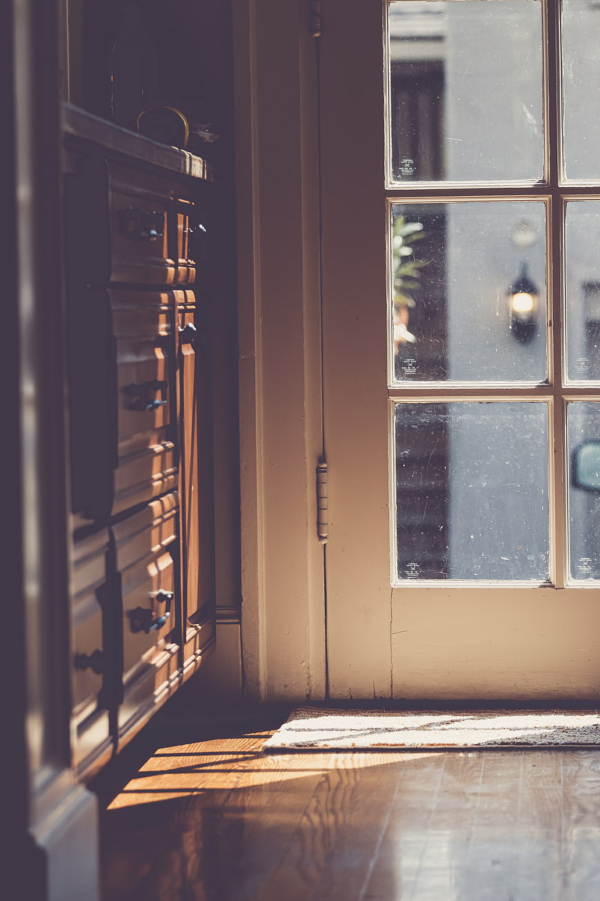 Sunlit wooden floor and vintage dresser near glass door