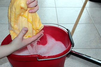 Hands wringing yellow cloth in red bucket of soapy water