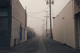 Foggy industrial alleyway with power lines and concrete buildings