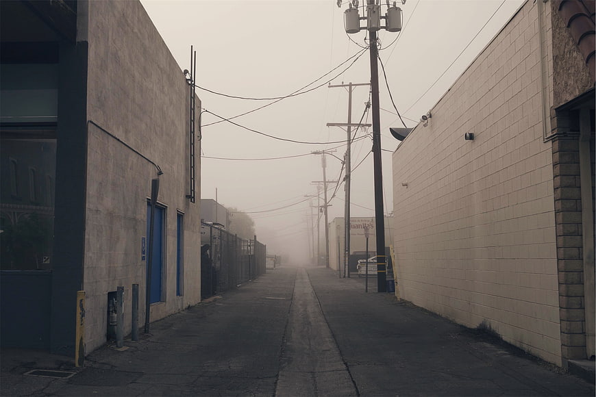 Foggy industrial alleyway with power lines and concrete buildings