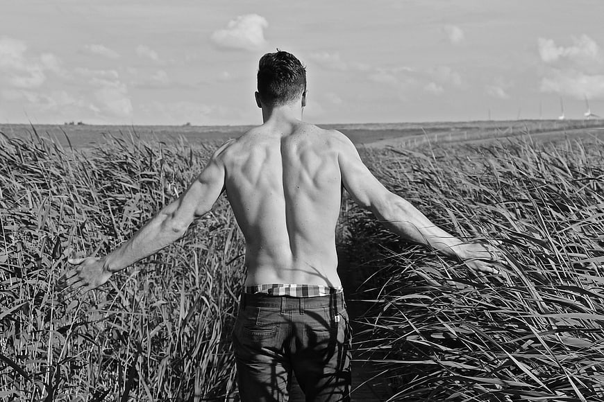 Shirtless Man Standing in Tall Grass Field