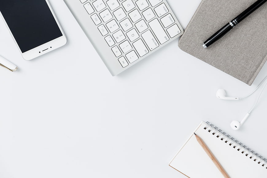 Minimalist white workspace with keyboard, smartphone, and notebook