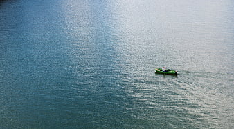 Aerial view of a lone green boat on a vast blue lake