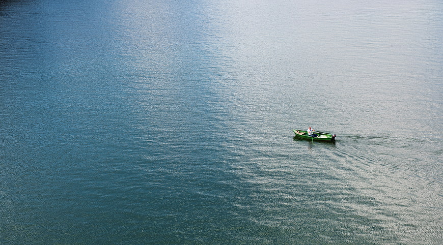 Aerial view of a lone green boat on a vast blue lake