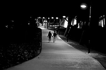 Couple walking hand in hand on a park path at night
