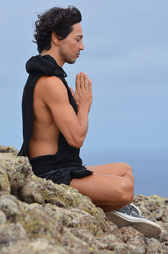 Man meditating on rocky cliff with ocean background