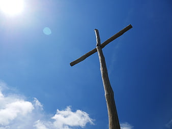 Rustic Wooden Cross Against Blue Sky with Sun