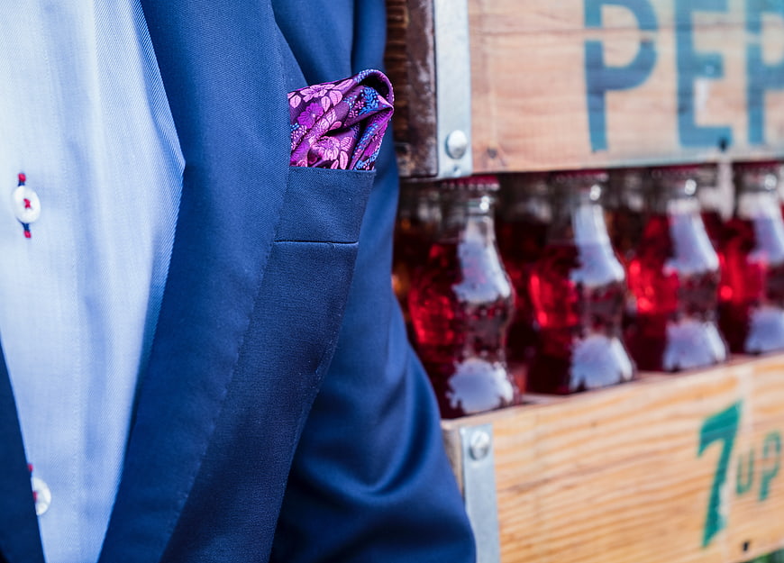 Close-up of blue suit with purple pocket square and vintage soda bottles