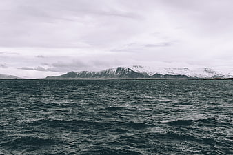 Snowy Mountains Across Dark Ocean Under Overcast Sky