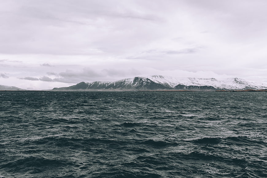 Snowy Mountains Across Dark Ocean Under Overcast Sky