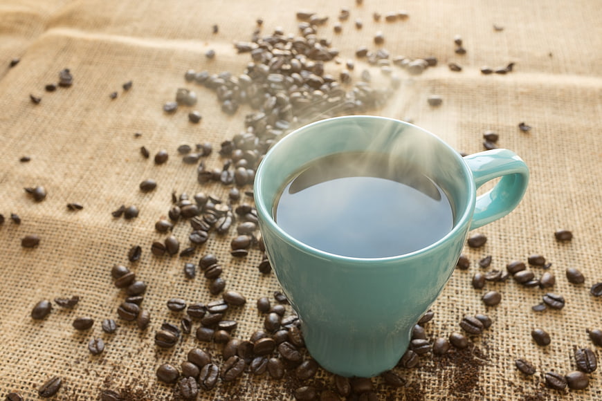 Steaming Blue Coffee Cup on Burlap with Scattered Beans
