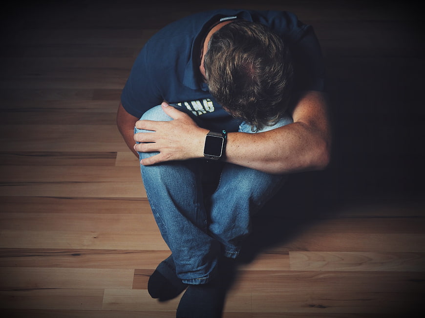 High angle view of depressed man sitting on wooden floor