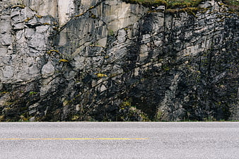 Asphalt road with yellow line against rocky cliff face
