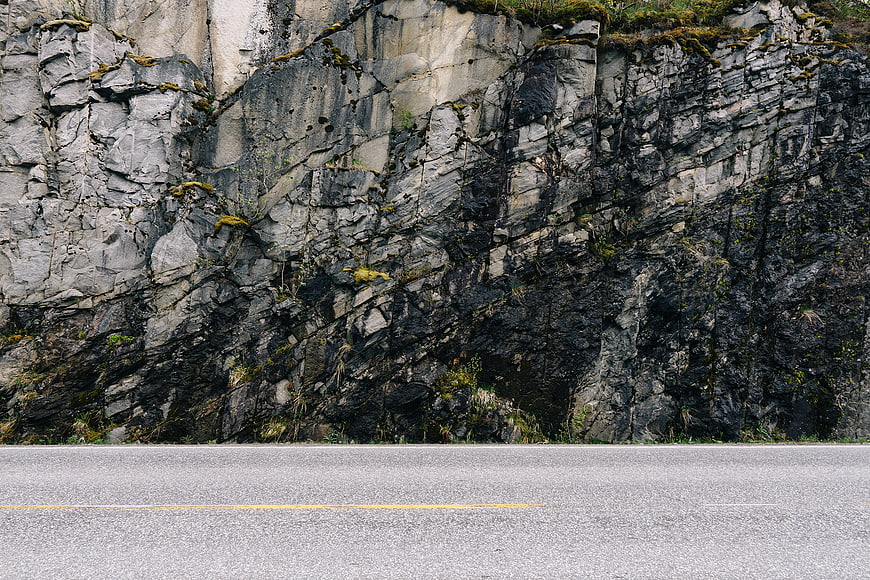 Asphalt road with yellow line against rocky cliff face
