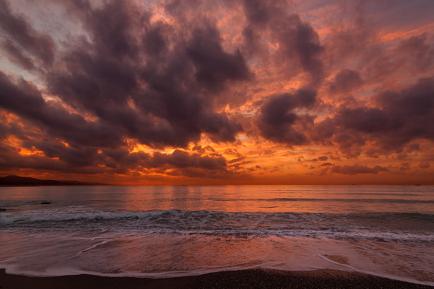 Dramatic Orange Sunset Over Ocean Waves and Beach