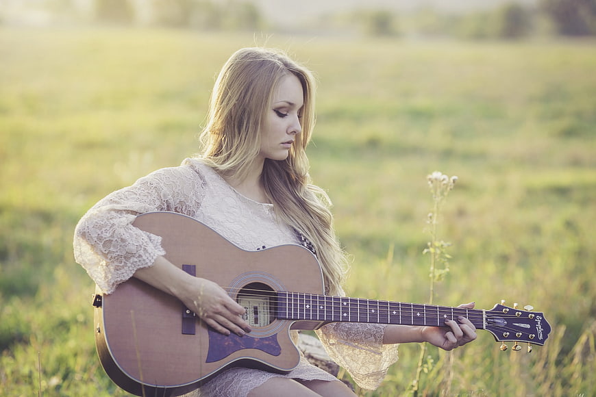 Woman Playing Acoustic Guitar in Grassy Field