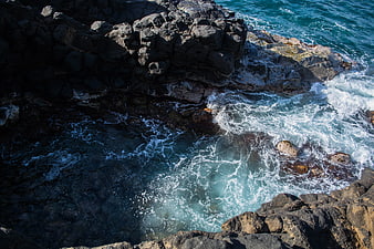 Aerial view of turquoise waves crashing against dark volcanic rocks