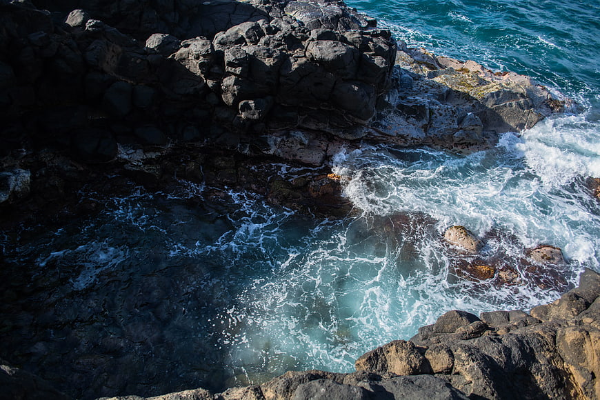 Aerial view of turquoise waves crashing against dark volcanic rocks