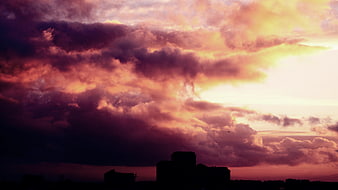Dramatic purple and orange sunset clouds over city silhouette