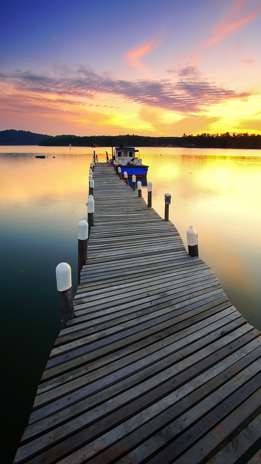 Wooden pier extending into calm water at sunset with boat