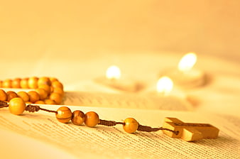 Wooden rosary on open Bible with lit candles