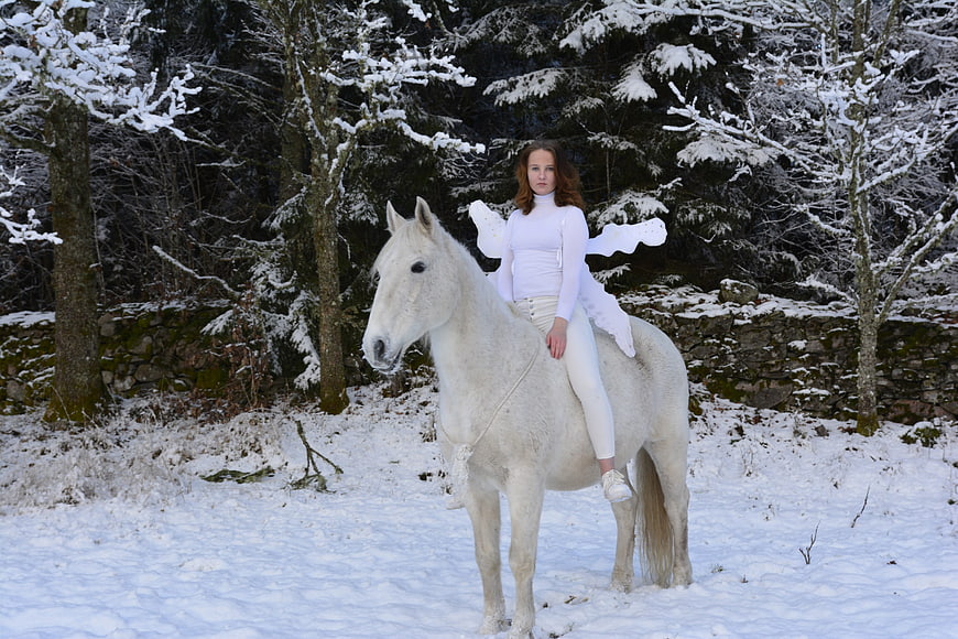 Woman with Fairy Wings Riding White Horse in Snowy Forest