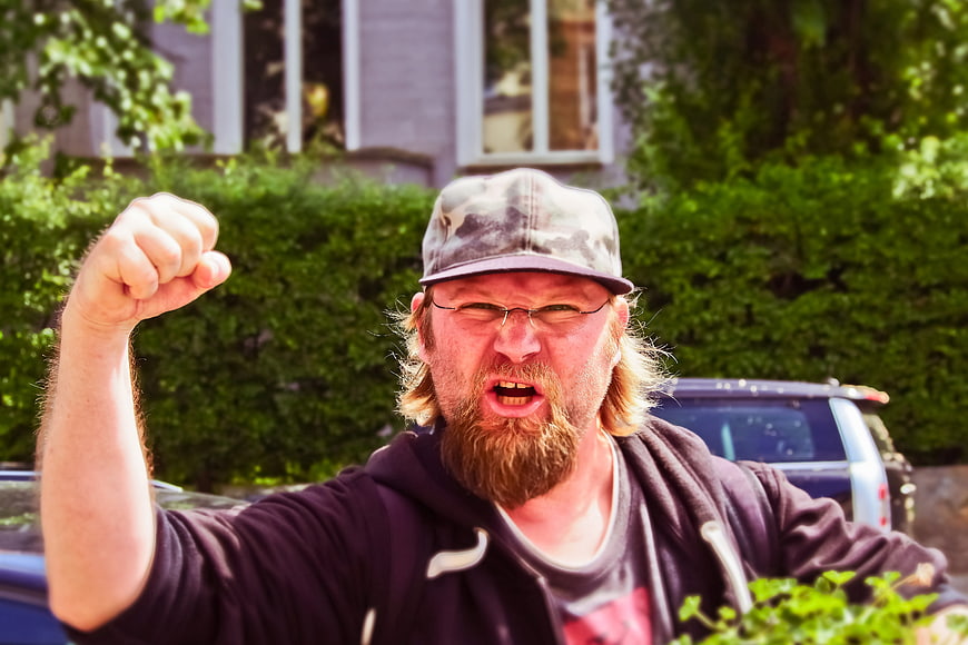 Angry bearded man shouting with raised fist in suburban neighborhood