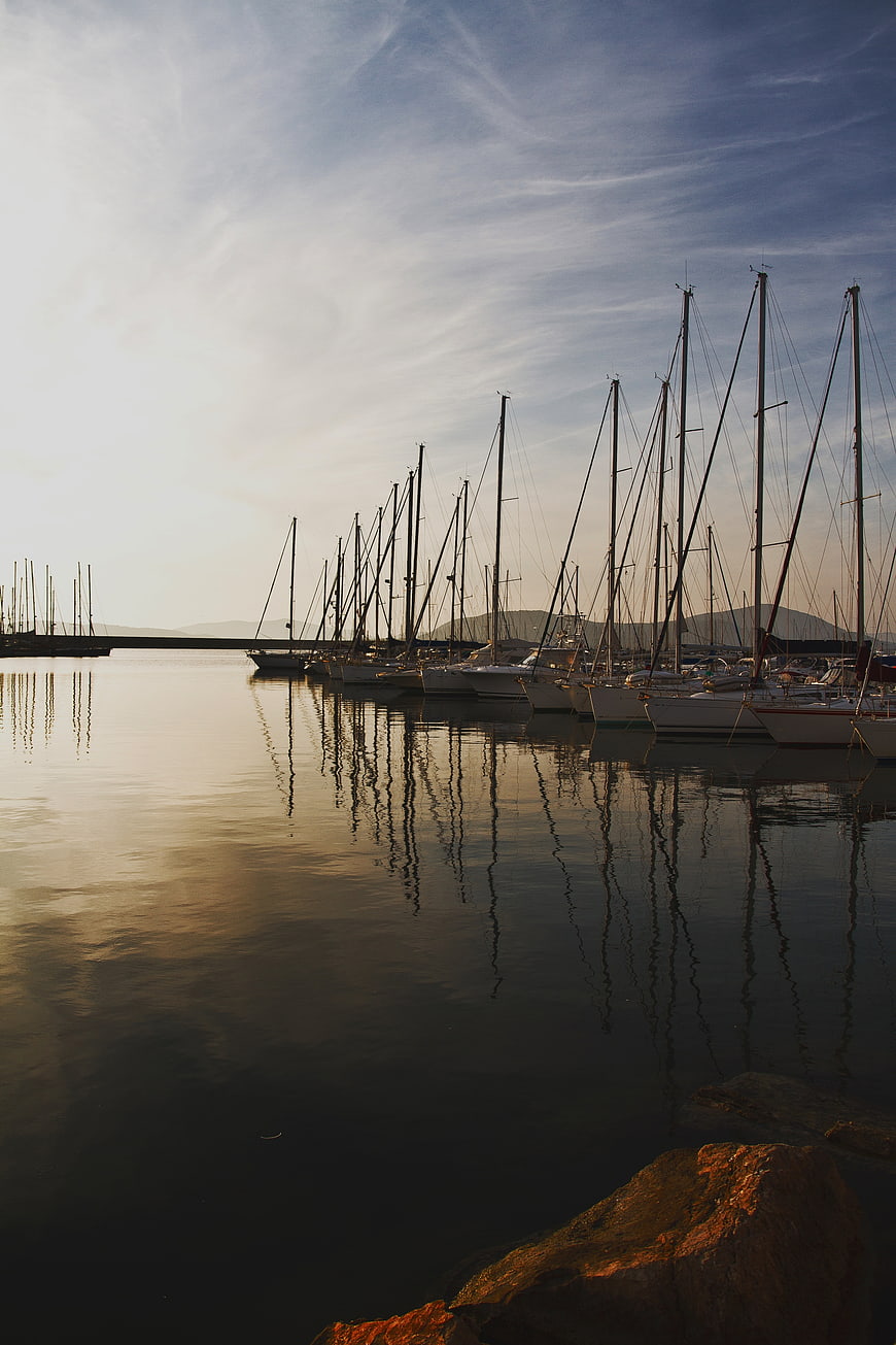 Sailboats docked in calm harbor at golden hour