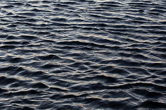 Dark rippling ocean water texture with golden sunset reflections