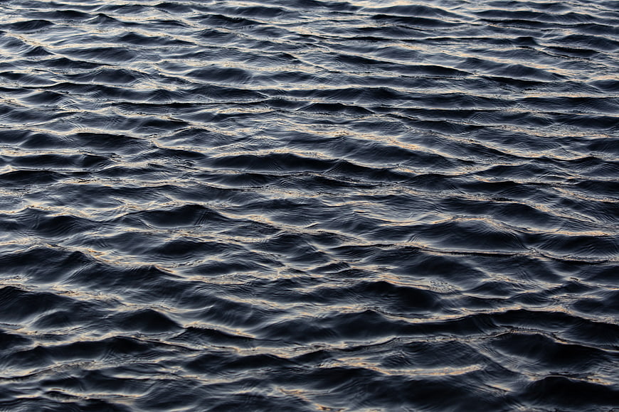Dark rippling ocean water texture with golden sunset reflections