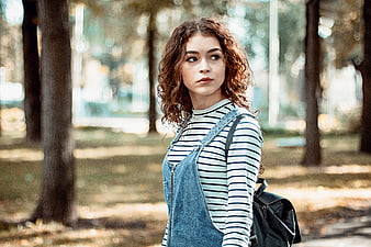 Young woman with curly hair in denim overalls outdoors