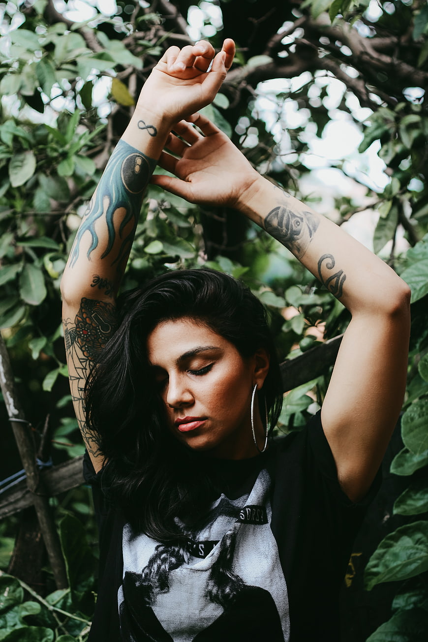 Woman with tattoos raising arms in nature