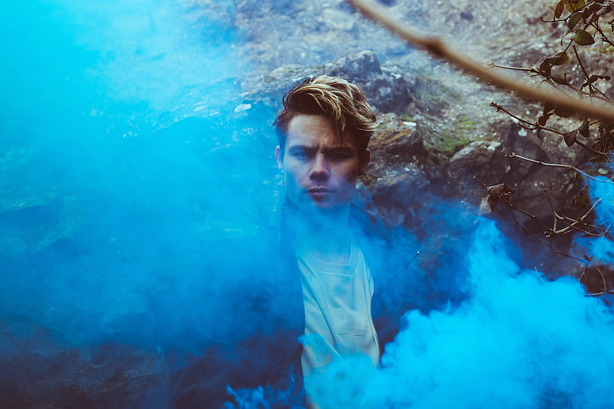 Young man with blue smoke in rocky outdoor setting
