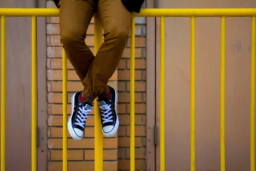Person sitting on yellow railing wearing sneakers