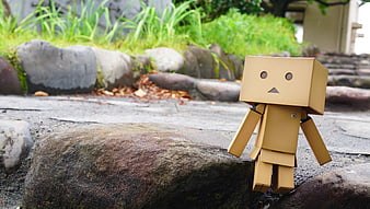 Cardboard robot toy standing on a large rock in a garden