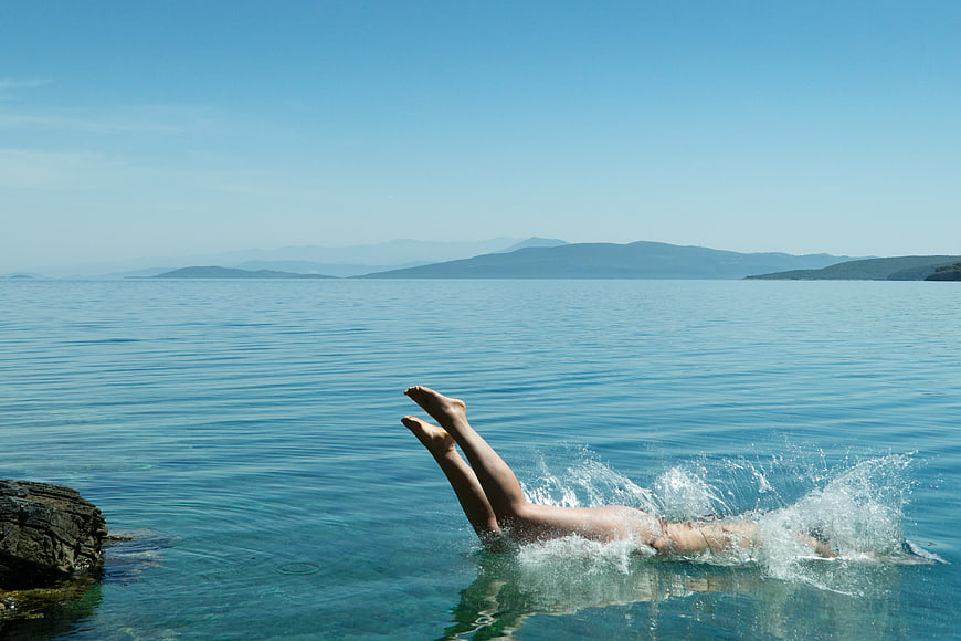 Woman diving into clear blue sea water with legs up
