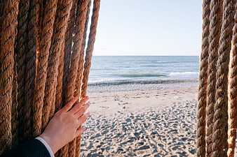 Hand parting thick ropes to reveal a sunny beach and ocean view