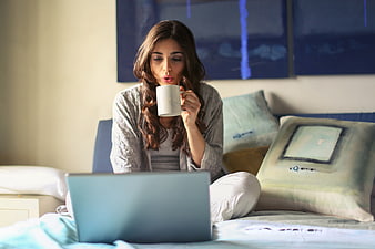 Woman drinking coffee in bed while using laptop