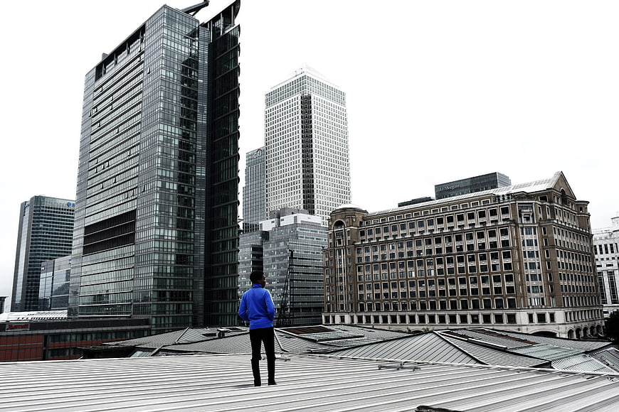 Man in Blue Jacket Standing on Rooftop Looking at City Skyline