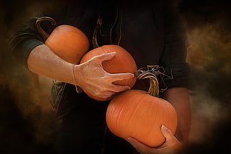 Woman holding three orange pumpkins in autumn